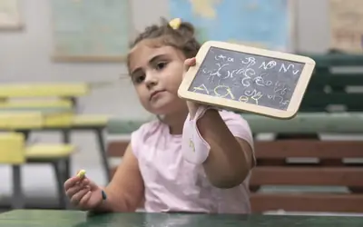 Κορίτσι δείχνει μια παλιά σχολική πλάκα με γράμματα στην αναπαράσταση της παλιάς τάξης
