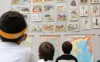 Παιδιά παρατηρούν εκπαιδευτικούς πίνακες με ζώα και χάρτη της Ελλάδας στην παλιά τάξη του μουσείου